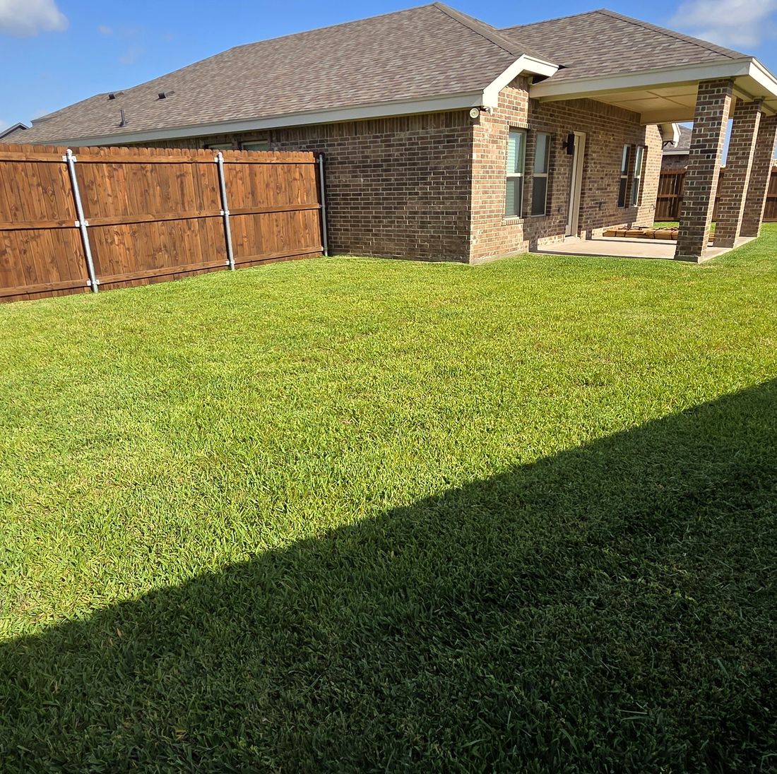 Brick home with a freshly cut, striped backyard by RGV Elite Lawn Care
